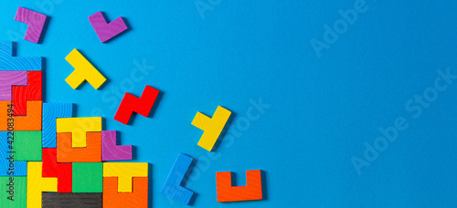 Different colorful shapes wooden puzzle blocks on light blue background. Geometric shapes in different colors, top view, copy space