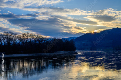 The sun disappearing behind the hills reflecting in the Danube river in Austria