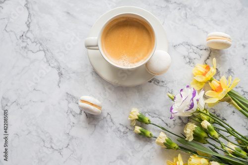 Macaroons with white cup of coffee, bright beautiful flowers on marble background.Beautiful breakfast for woman. Spring concept.Copy space