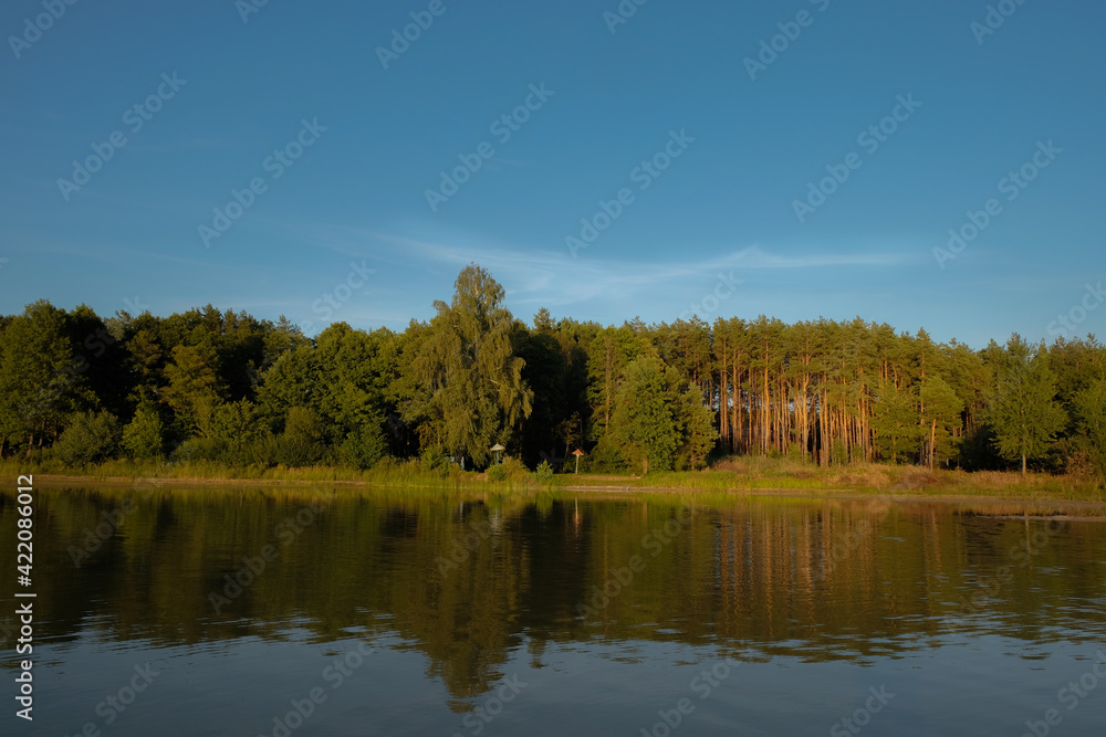 Wonderful evening golden hour over the lake. The forest is reflected in clear water. Lake Svityaz. Shatsky National Natural Park. Ukraine.