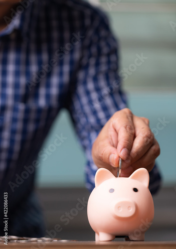 Vertical business man hand putting coins into the piggy bank, saving money concept.