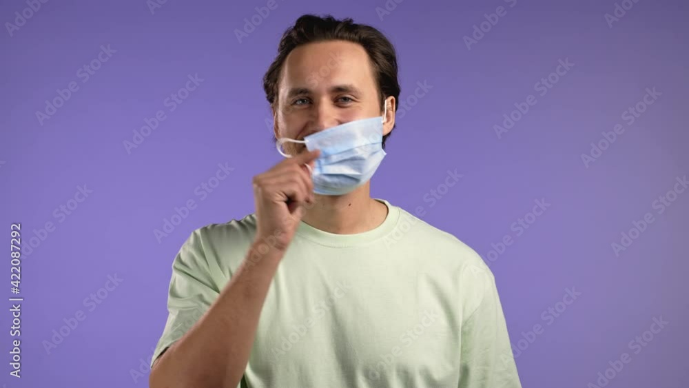 Pleased man removed protective mask as symbol of pandemic, epidemic end. Violet studio background Pleased man removed protective mask as symbol of pandemic, epidemic end. Violet studio background