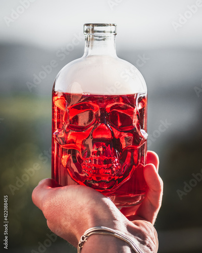 bottiglietta a forma di teschio umano con liquido rosso tenuta in mano photo