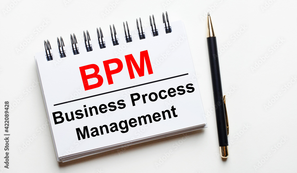 On a light background, a white notebook with are words BPM Business Process Management and a pen.