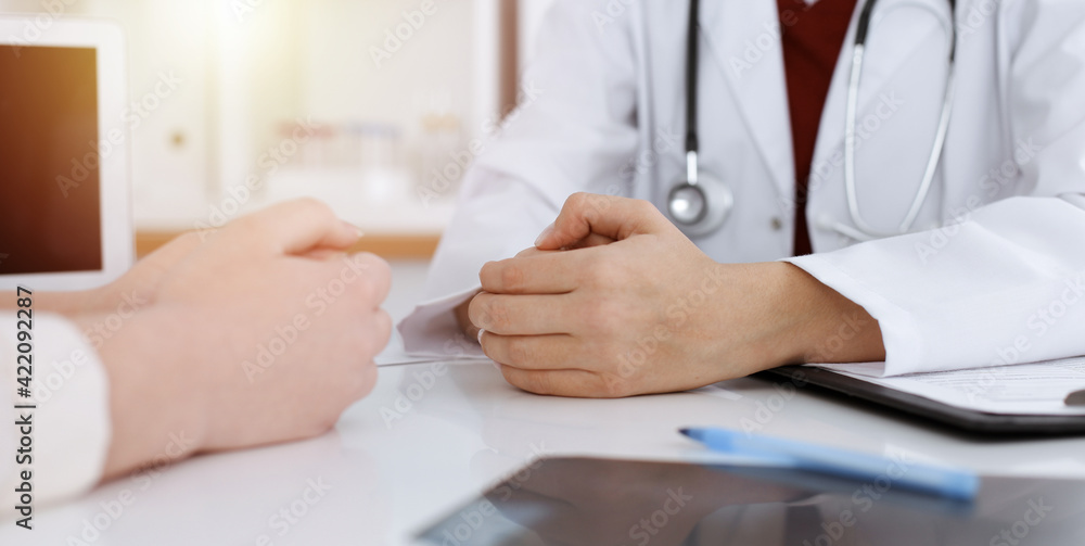 Unknown woman-doctor and patient discussing something while sitting at the table in sunny clinic, close-up Unknown woman-doctor and patient discussing something while sitting at the table in sunny clinic, close-up