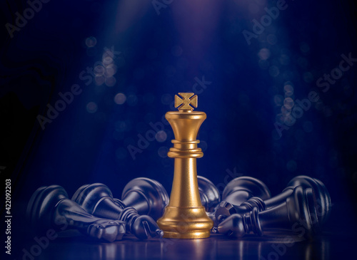 Golden king chess stand which flare light surrounded by falling around silver chess pieces to fighting with teamwork to victory, business strategy concept and leader and teamwork concept for success.