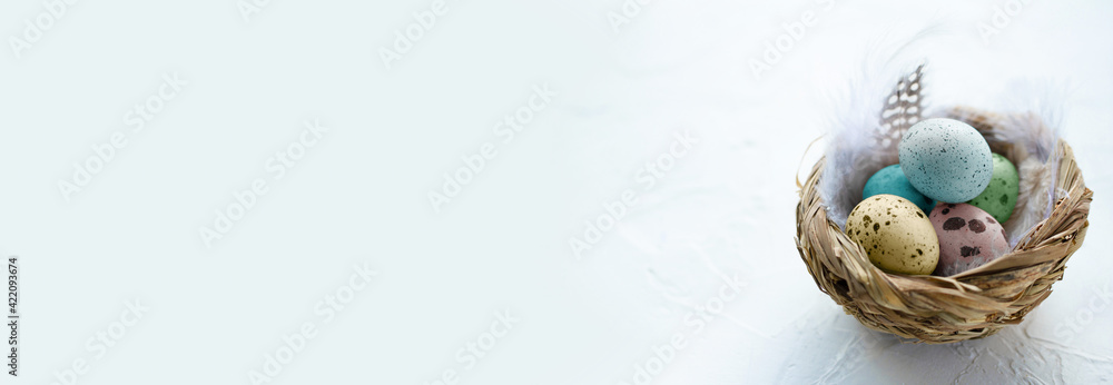Colorful Easter eggs in the small nest with feathers on a light background. Copy space. Banner. The Easter concept. Happy Easter Colorful Easter eggs in the small nest with feathers on a light background. Copy space. Banner. The Easter concept. Happy Easter