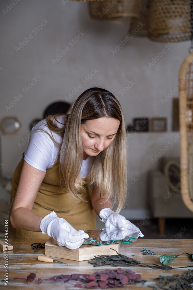 The process of decorating do it yourself. woman works with flowers in a small home workshop. Entrepreneurs lifestyle concept. wooden frames with botanical plants The process of decorating do it yourself. woman works with flowers in a small home workshop. Entrepreneurs lifestyle concept. wooden frames with botanical plants