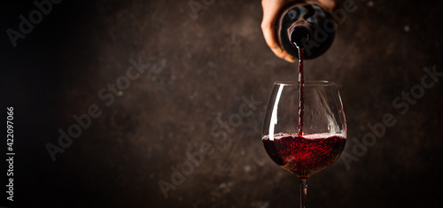 Pouring red wine into the glass against rustic dark wooden background © petrrgoskov