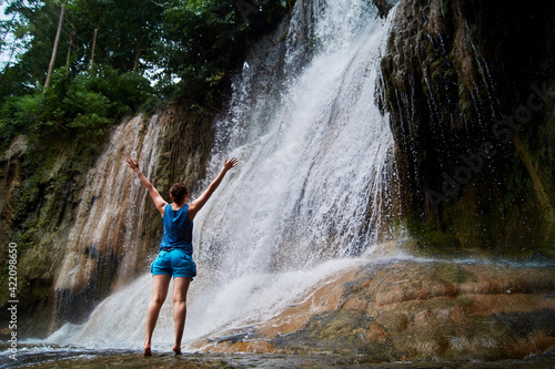 A girl stands barefoot on tiptoe on wet stones at a waterfall in the jungle of Thailand © Anastasiia