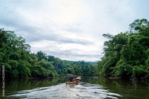 A fishing boat floats on a river in the green jungle in Thailand © Anastasiia