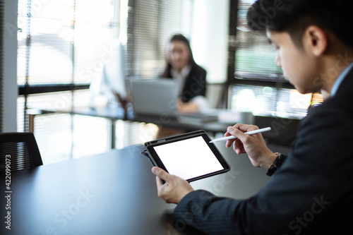 A young Asian businessman works at his office. And use the phone and tablet with a blank screen