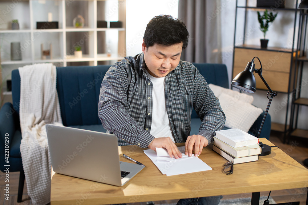 Asian man making paper plane while sitting at desk with laptop Asian man making paper plane while sitting at desk with laptop