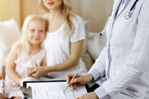 Doctor and patient. Pediatrician using clipboard while examining little girl with her mother at home. Happy cute caucasian child at medical exam. Medicine concept