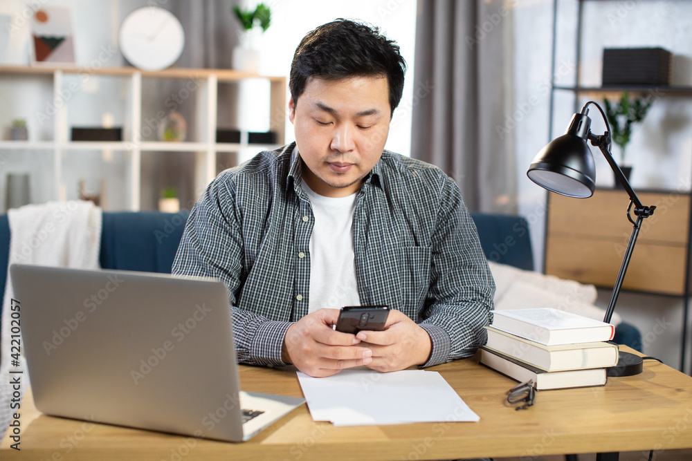 Fototapeta premium Asian male employer sitting at table and using gadgets