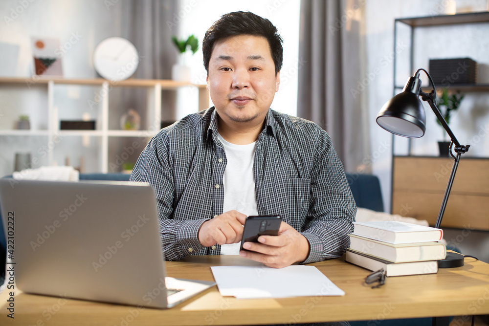 Pleasant Asian male worker sitting at table and using gadgets Pleasant Asian male worker sitting at table and using gadgets
