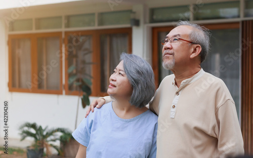 Happy retired senior Asian couple standing in front of the house with happy smiley face. Portrait of healthy old retired people