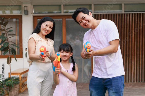 Young adult Asian family having fun playing water gun on play yard, Songkran holiday in Thailand. Thai traditional holiday on April, summer holiday of thailand photo