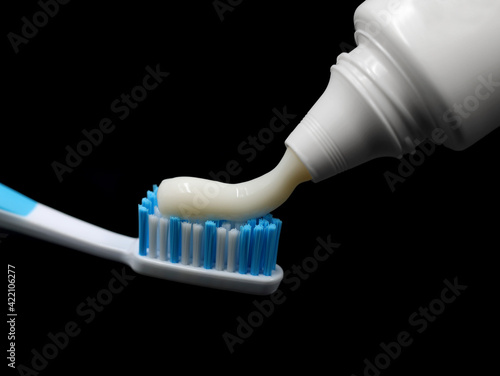 Toothpaste is squeezed out of the tube onto a blue toothbrush, isolated on black background