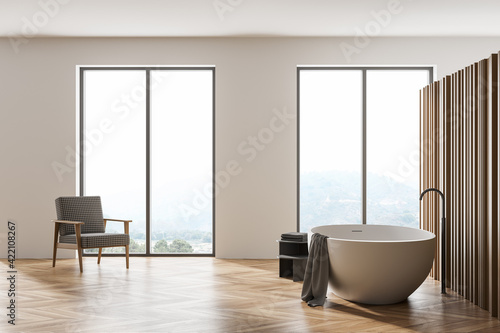 Wooden bathroom interior with armchair  bathtub on parquet floor and windows