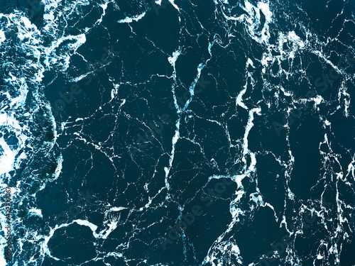 Full frame aerial view of ocean surface and waves - natural abstract dark blue background. Trendy cinematic color grading.