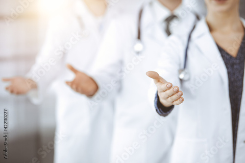 Doctors standing as a team while offering helping hand for shaking hand or saving life in sunny clinic. Medicine concept