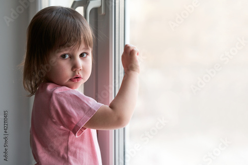 A little girl in home clothes at the window. Children's portrait.