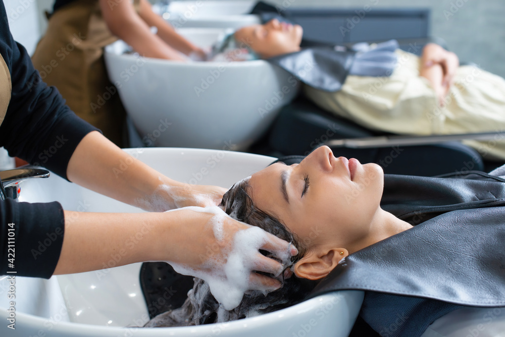 Beauty and people concept. Woman applying shampoo and massaging hair of a customer. Woman having her hair washed in a hairdressing salon. Beauty and people concept. Woman applying shampoo and massaging hair of a customer. Woman having her hair washed in a hairdressing salon.