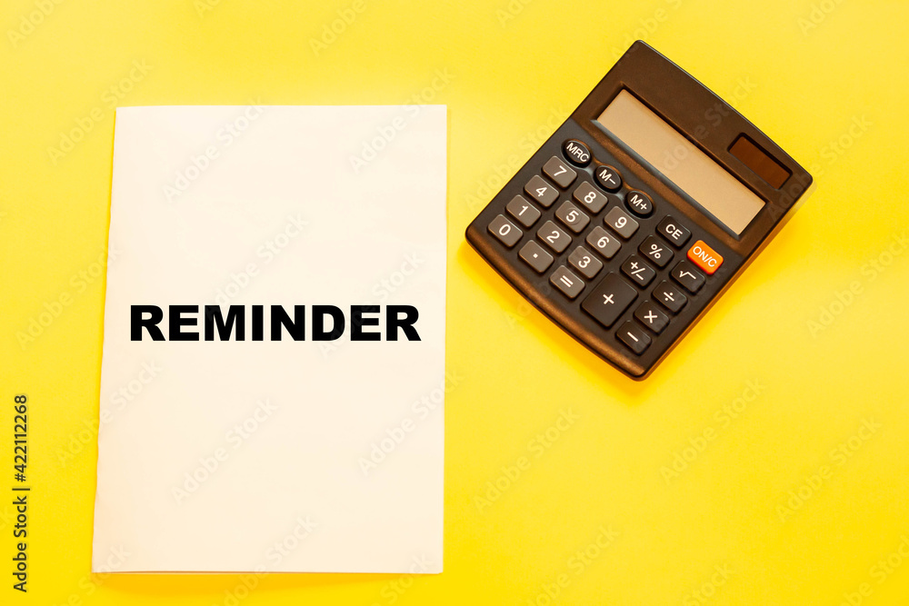 The word REMINDER on a white large sheet of paper on a yellow background with a calculator. The word REMINDER on a white large sheet of paper on a yellow background with a calculator.