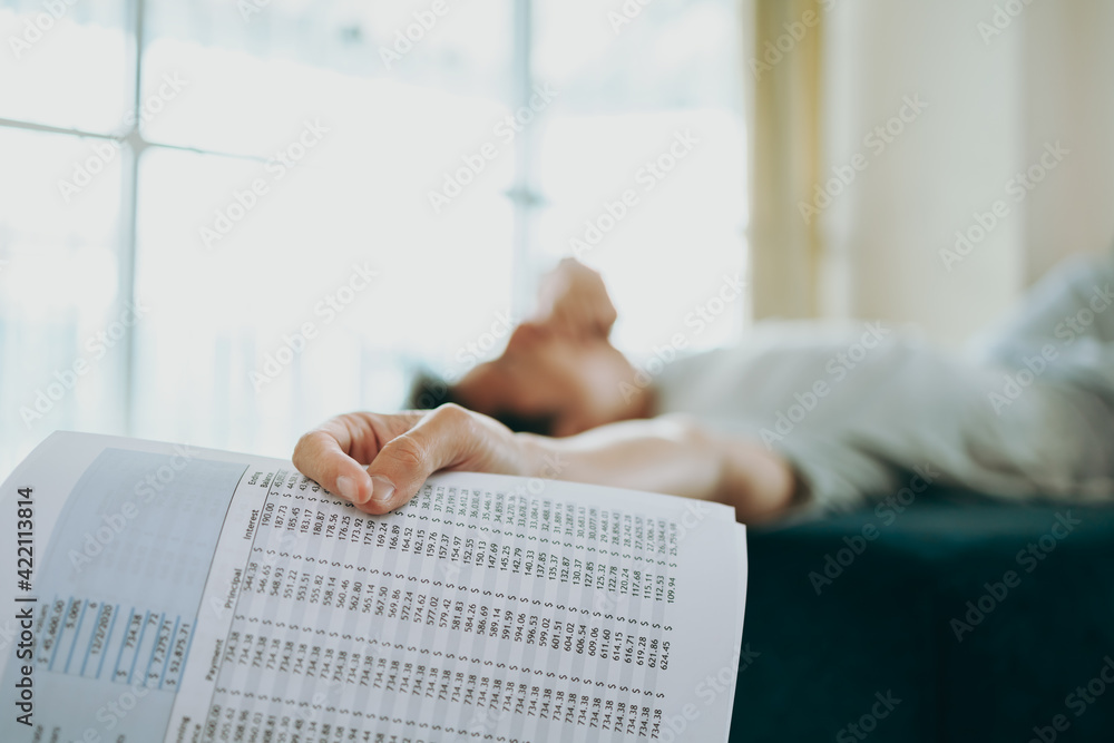 Naklejka premium Young Businessman working at home with paper graph and he is yawn on sofa. Business and freelance concept.