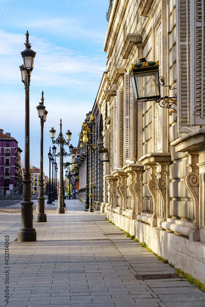 Sidewalk of the street of the Royal Palace of Madrid with street lamps and old building in sunny day.