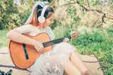 Girl wearing headphone to listen music and playing guitar in the forest. Music hobby and picnic concept.