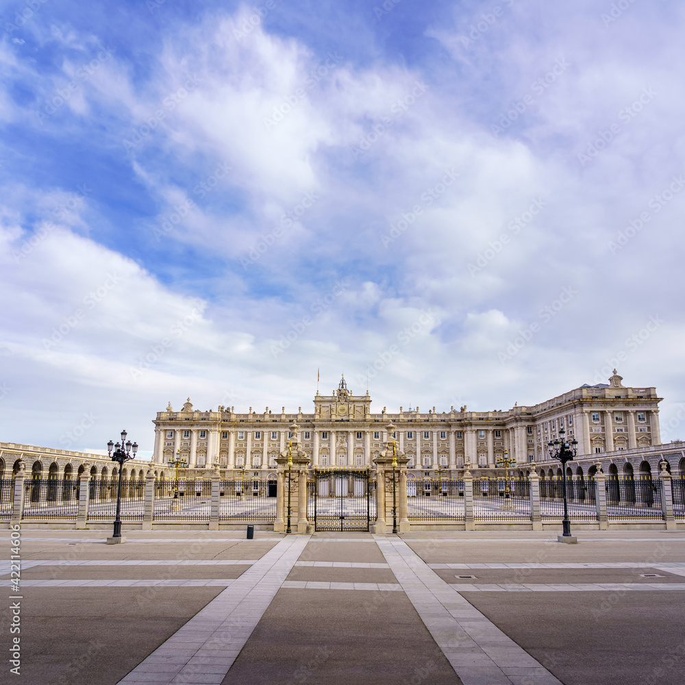 Main facade of the royal palace of Madrid with its huge esplanade and blue sky with clouds at sunrise.