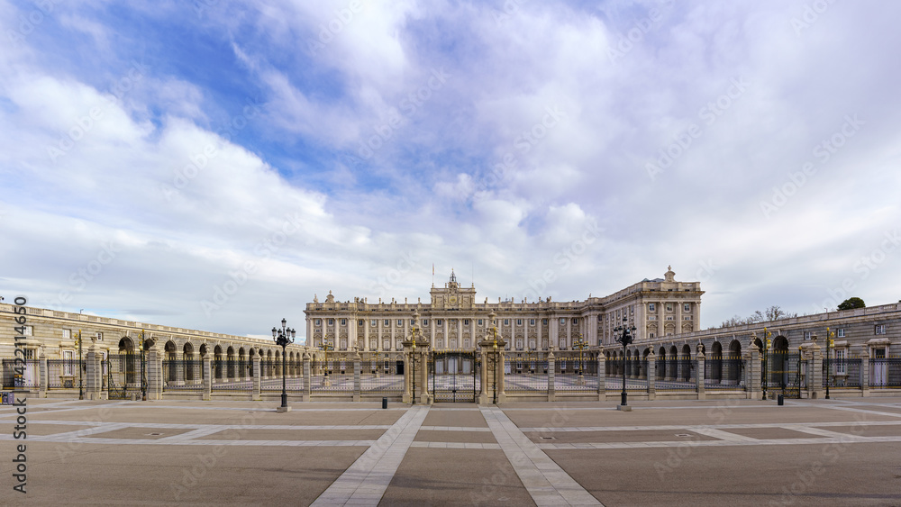 Main facade of the royal palace of Madrid with its huge esplanade and blue sky with clouds at sunrise.