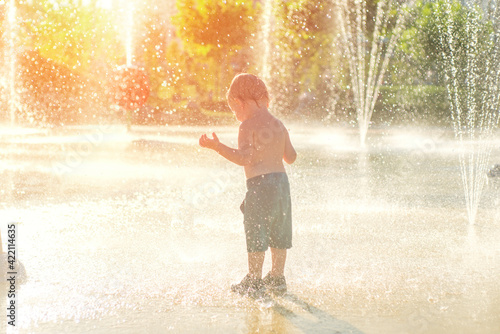 Happy child has fun playing in water fountains on hot day during summer. Boy playing in water at waterpark. A kid in spray park
