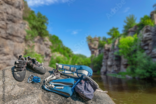 Climbing gear equipment on rock on blurred river canyon background. Climb shoes, belaying carabiners, loops, ropes, bag for magnesia, belay system.
