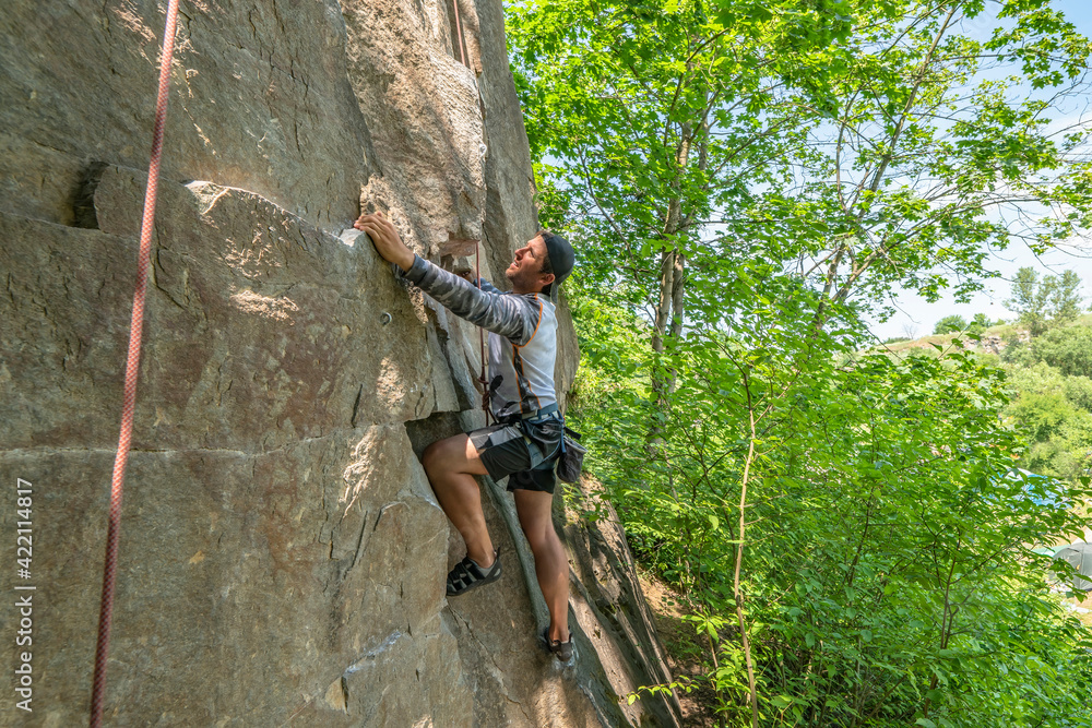 Obraz premium Man climber with climbing gear equipment climbs on rock wall. Canyon rocks in green forest