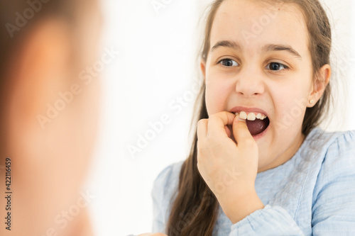A loose baby tooth falls out in a little girl with an open mouth