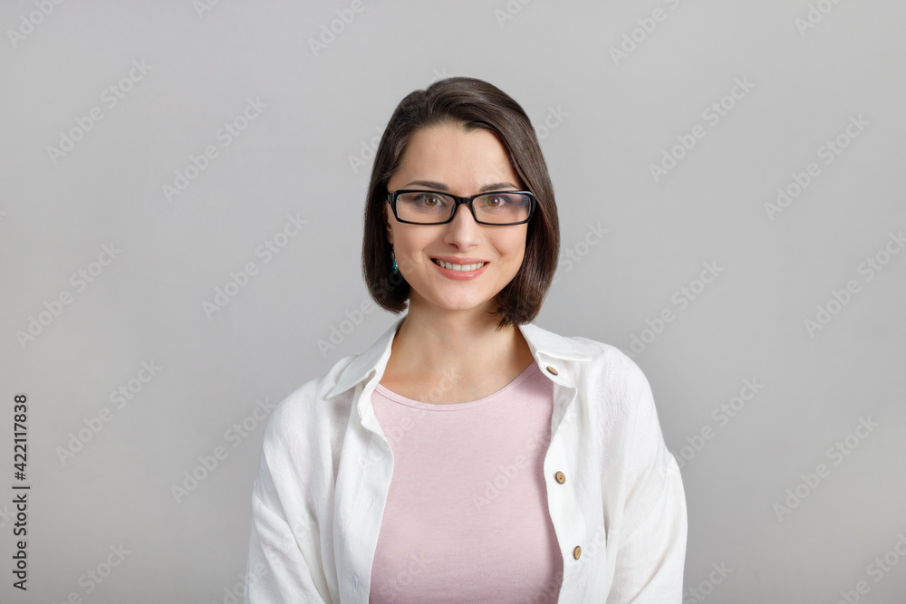 Portrait of mixed race, cheerful, modern, stylish, cute, clever, smiling woman in glasses on grey background, looking at camera