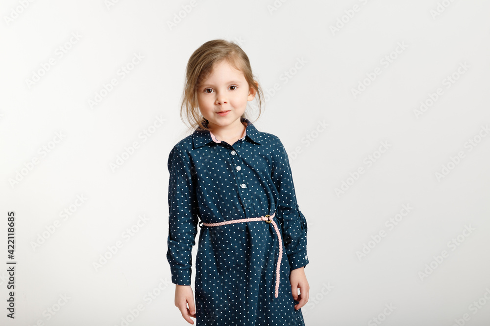 Little sweet caucasian fashion girl 4-6 years old wearing a blue dress with polka dots stands on a white background. Little sweet caucasian fashion girl 4-6 years old wearing a blue dress with polka dots stands on a white background.