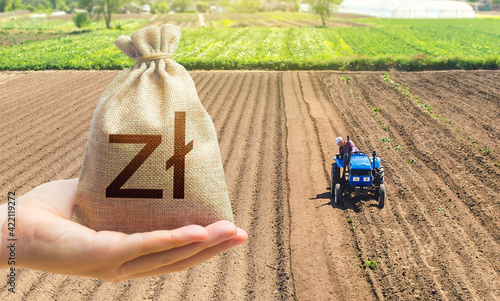 Hand with a polish zloty money bag on the background of a farm field with a tractor. Land lease, land market. Investments in agriculture and agribusiness. Subsidies support for agricultural producers. photo