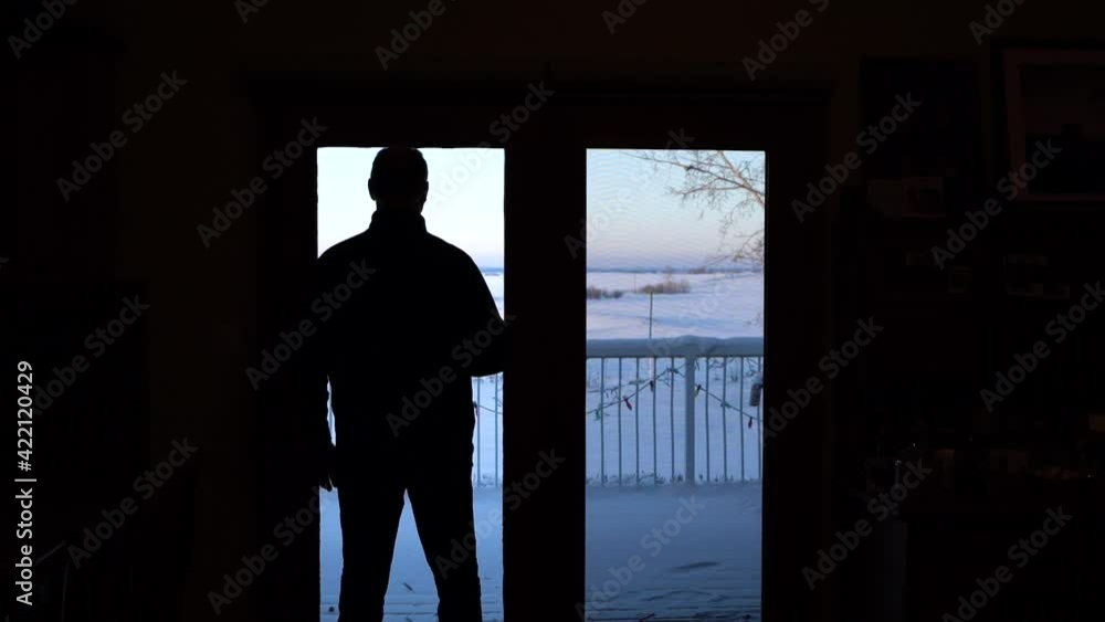 Silhouette of the back of a thoughtful man looking at a snowy winter landscape through the window. Silhouette of the back of a thoughtful man looking at a snowy winter landscape through the window.