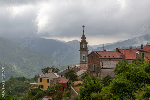 The bell tower of the temple against the background of mountains, surrounded by houses with tiled roofs. Low clouds after rain.
