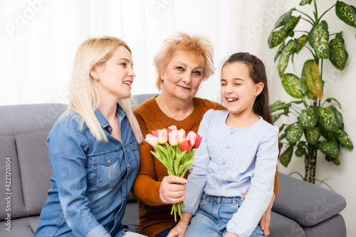 Photo portrait of granddaughter congratulating granny giving tulips bunch sitting near mom