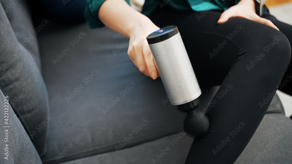 Woman massaging leg with massage percussion device at home.