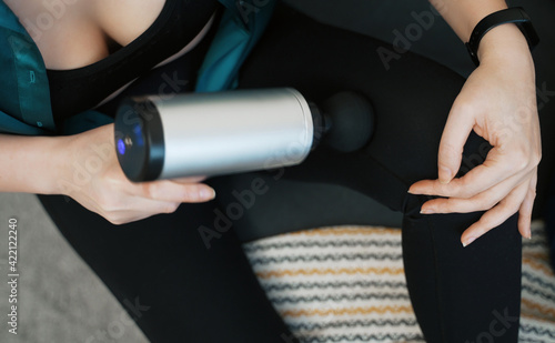 Woman massaging leg with massage percussion device at home.