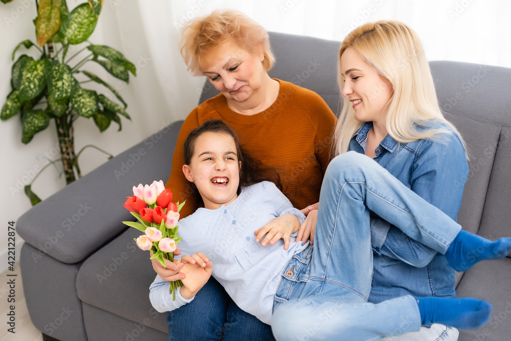 Photo portrait of granddaughter congratulating granny giving tulips bunch sitting near mom Photo portrait of granddaughter congratulating granny giving tulips bunch sitting near mom