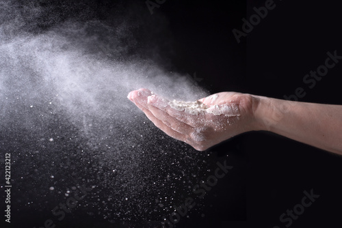 Wheat flour flying in the wind with female hands on a black background, spraying white powder.