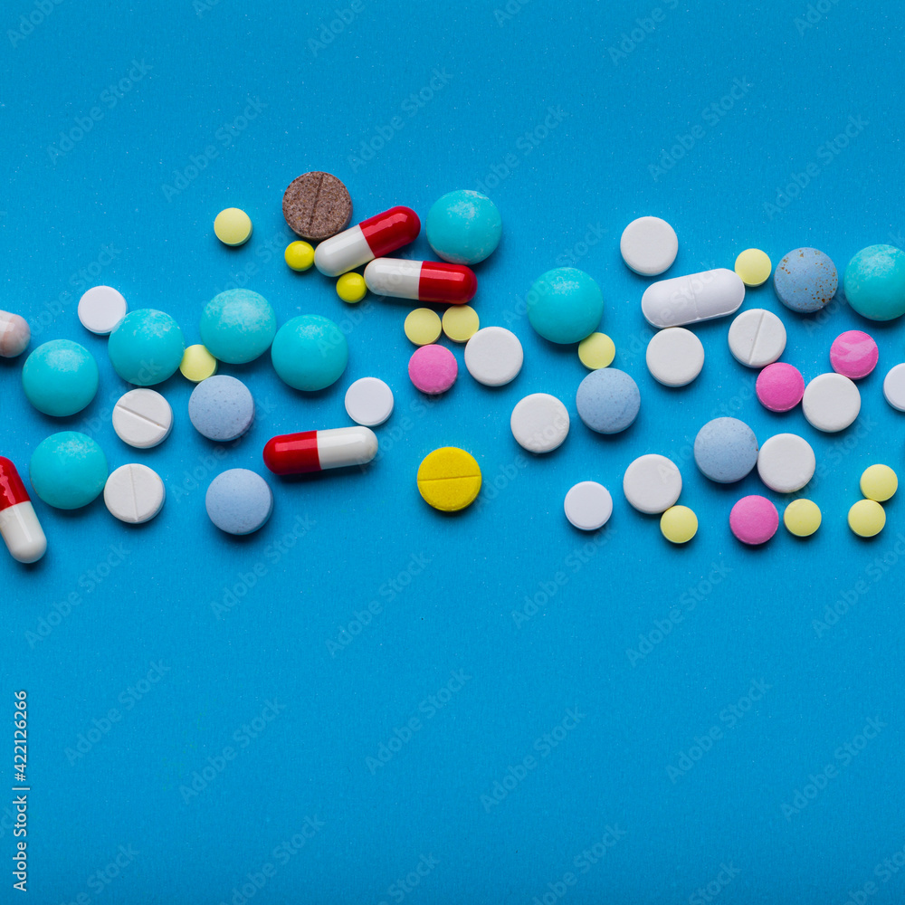 A lot of multicolored pills and capsules on a blue background as a concept of addiction from medicine. Vitamins to keep immunity on a high level. A lot of multicolored pills and capsules on a blue background as a concept of addiction from medicine. Vitamins to keep immunity on a high level.