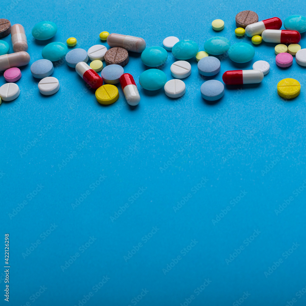 A lot of multi-colored pills on blue background with free space for text, as a concept of medical treatment with a prescription. Painkillers and antibiotics variation, allergy on medicine. A lot of multi-colored pills on blue background with free space for text, as a concept of medical treatment with a prescription. Painkillers and antibiotics variation, allergy on medicine.